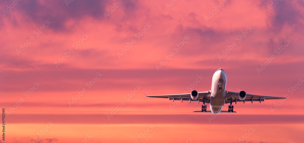 Airplane is flying in colorful sky at sunset. Landscape with white passenger airplane, purple sky wi