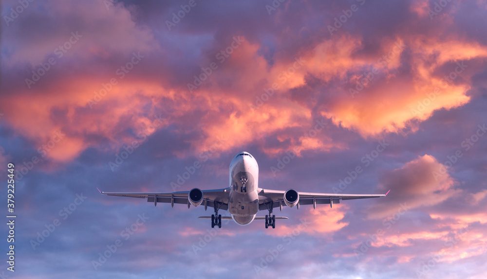 Airplane is flying in colorful sky at sunset. Landscape with white passenger airplane, purple sky wi