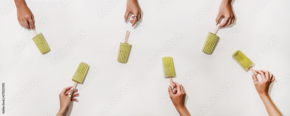 Green matcha coconut vegan ice cream popsicles. Flat-lay of womens hands taking matcha popsicles fro