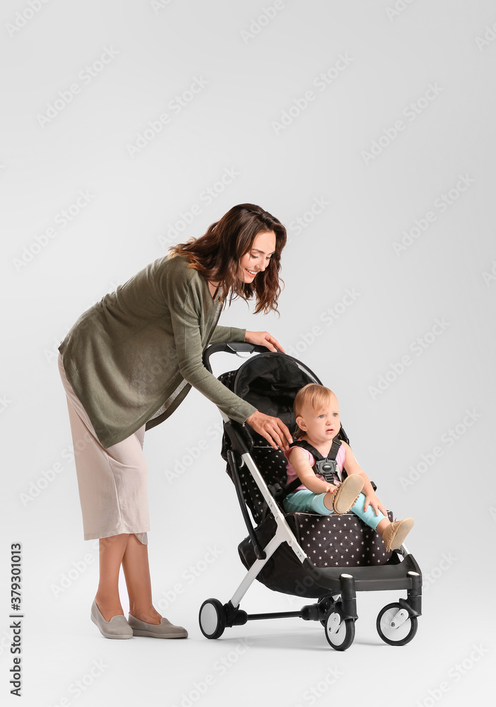 Woman and her cute baby in stroller on light background