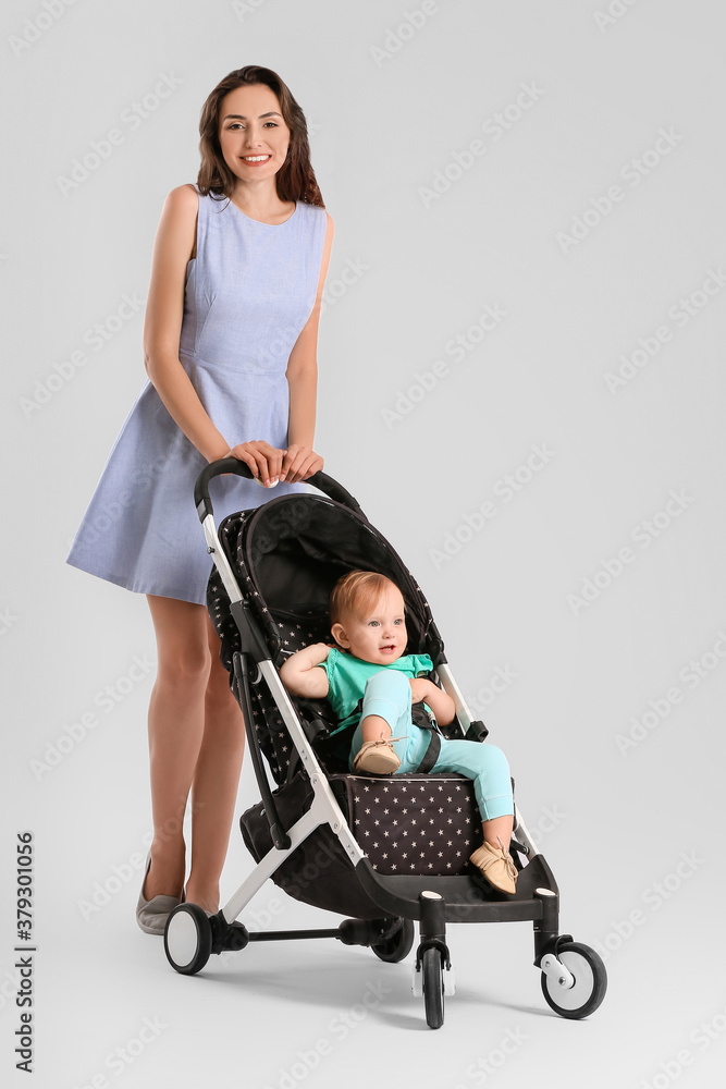 Woman and her cute baby in stroller on light background