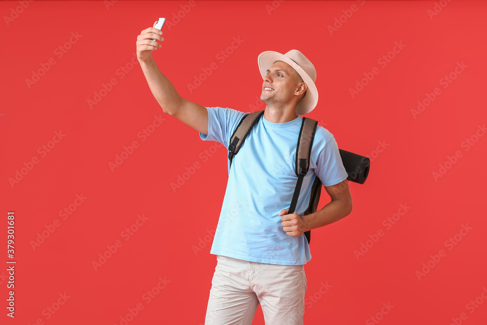 Male tourist taking selfie on color background