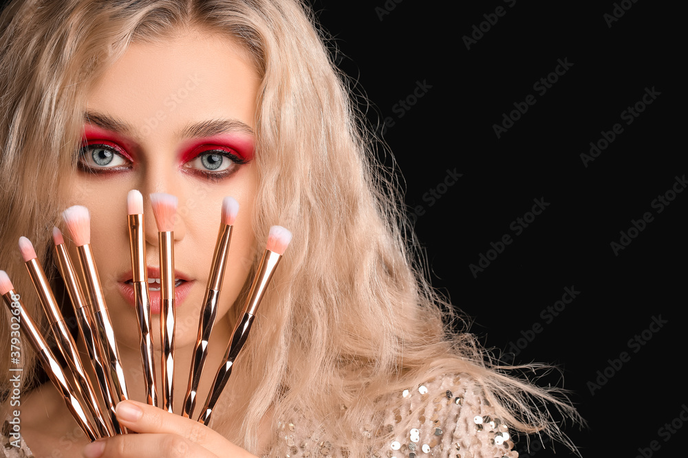 Young woman with beautiful eyeshadows and makeup brushes on dark background