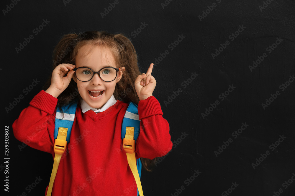 Little schoolgirl pointing at something on dark background