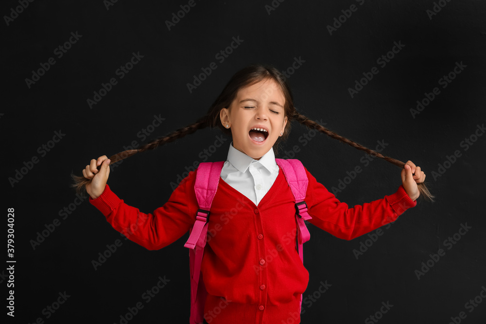 Grimacing little schoolgirl on dark background