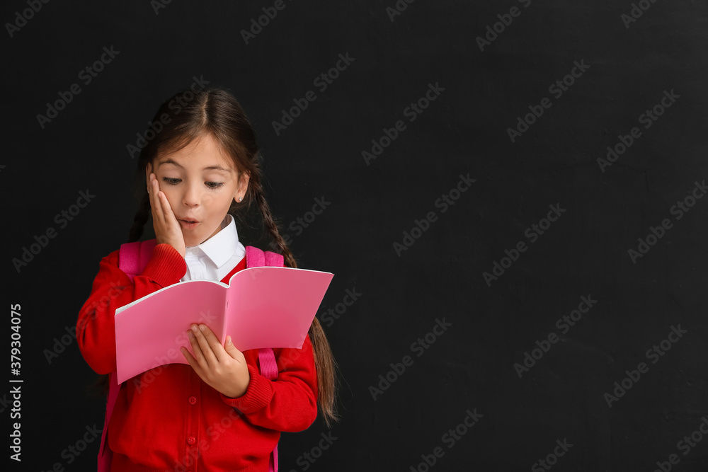 Little schoolgirl with copybook on dark background