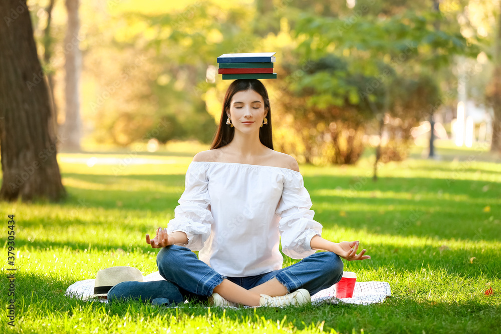 Beautiful young woman with books meditating in park