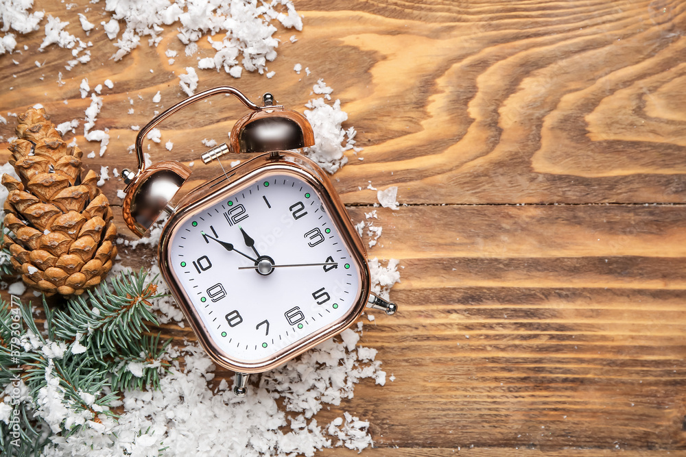 Alarm clock, snow, cones and fir branches on wooden background