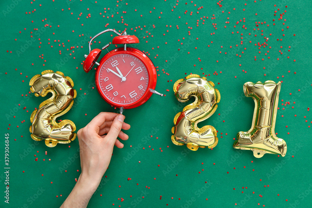 Hand, alarm clock and balloons in shape of figure 2021 on color background. New Year celebration