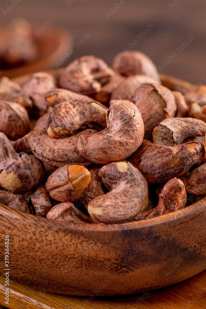 Cashew nuts with peel in a wooden bowl on wooden tray and table background, healthy raw food plate.