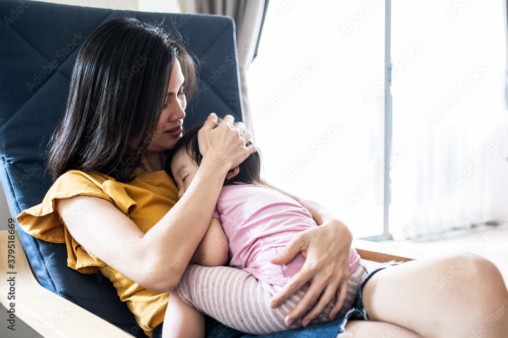 Asian mother hugging sleeping baby in her arms and kissing the kid. 