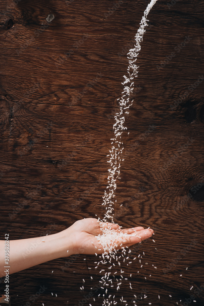 Dropping rice grain into hand isolated on wooden background