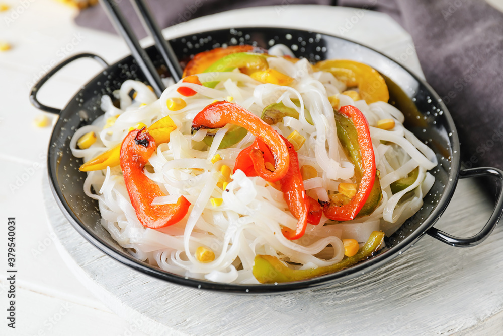 Frying pan with tasty rice noodles and vegetables on table