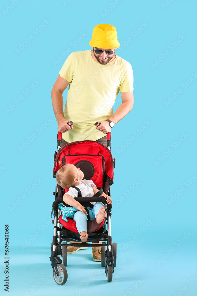 Father and his cute baby in stroller on color background