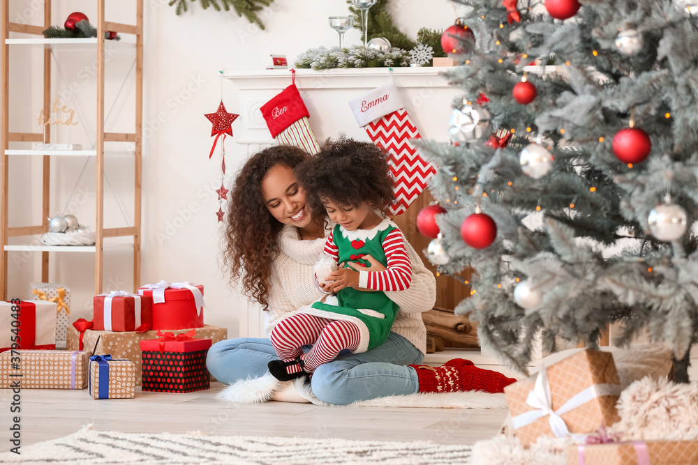 Cute African-American girl and her mother with Christmas gifts at home