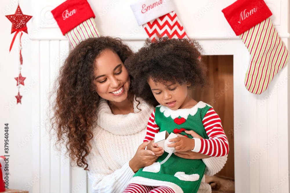 Cute African-American girl and her mother with Christmas gifts at home