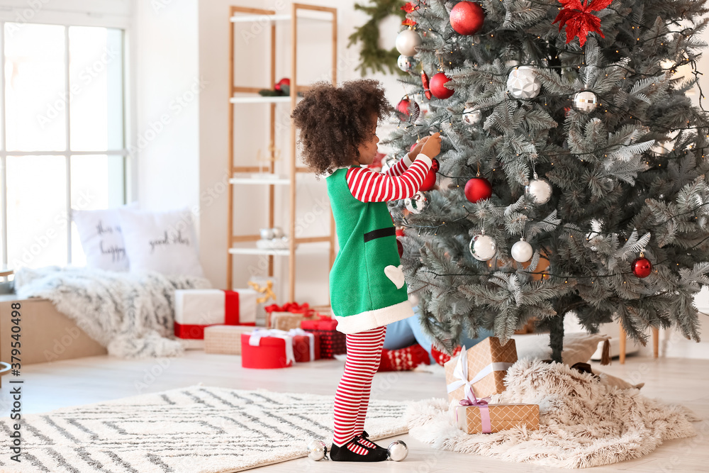 Cute African-American girl decorating Christmas tree at home