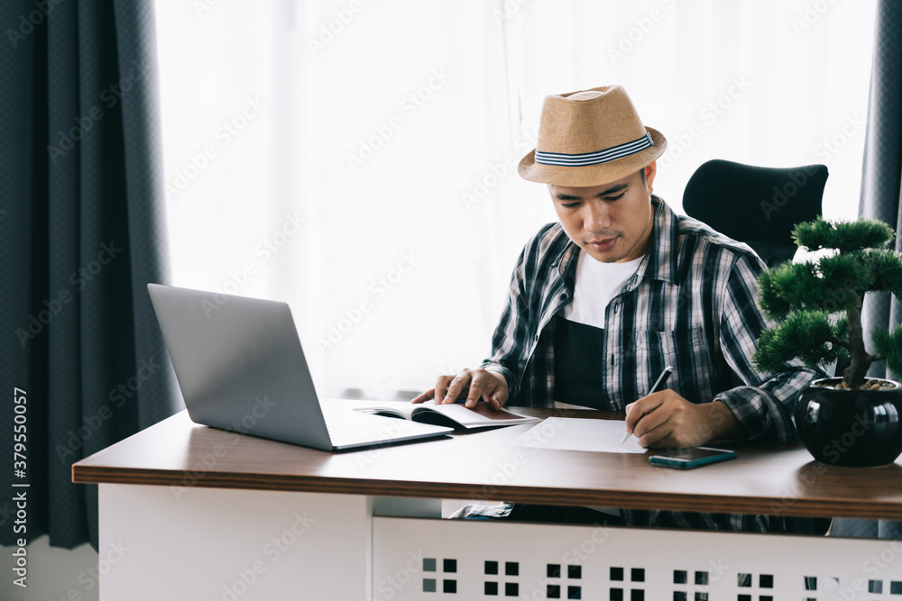 Asian young man sitting at his table reading and take notes and plan the work at home office, Stay h