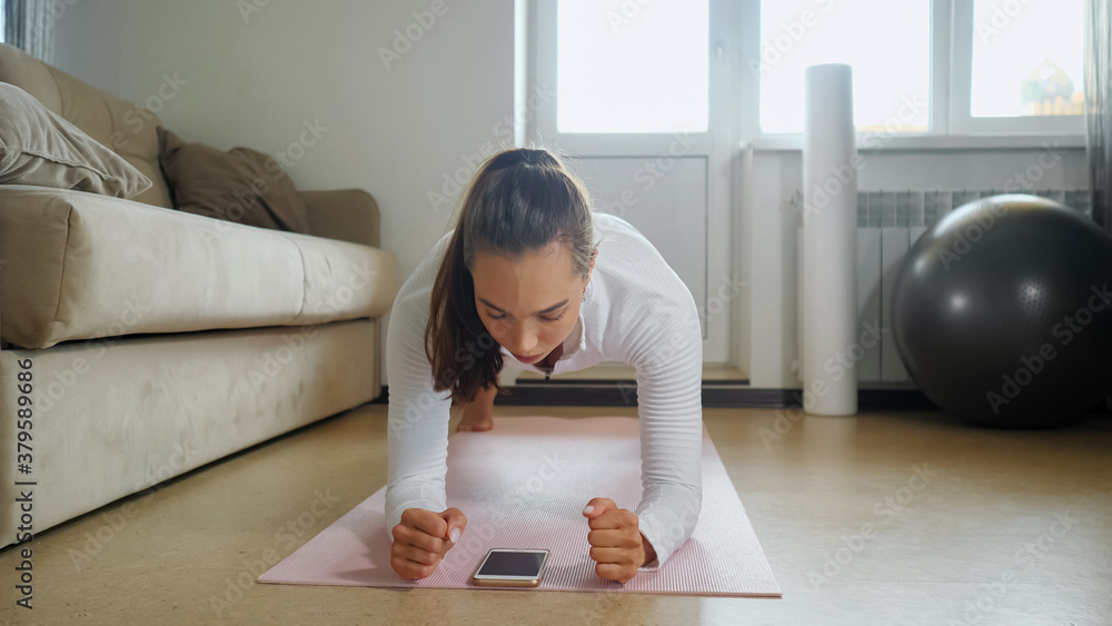 brunette woman in stylish tracksuit has intense training watching tutorial on modern mobile phone on