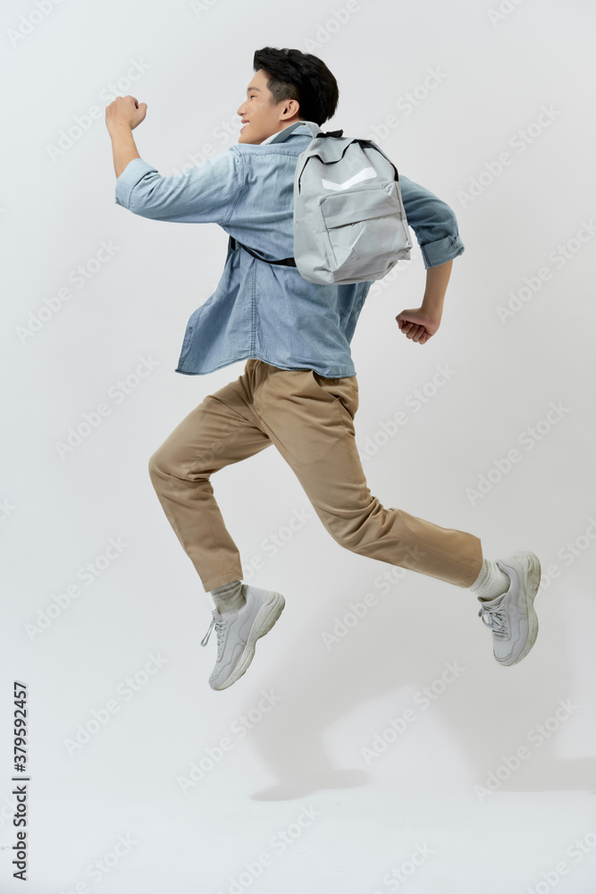 Happy young Asian student man jumping in the air with backpack over white background.