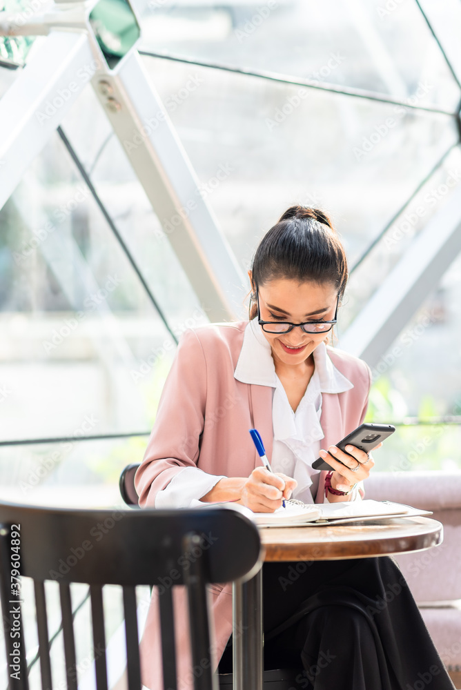 Business woman in pink suit note down information from smartphone in the morning