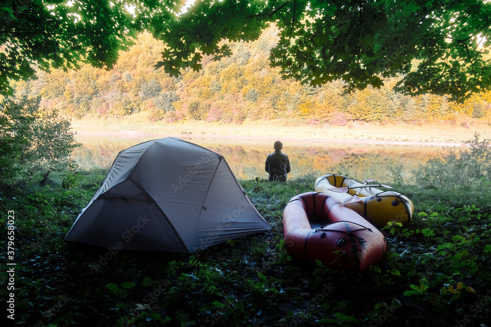 Man near tent and packrafts in forest camp near river. Packrafting. Active lifestile concept