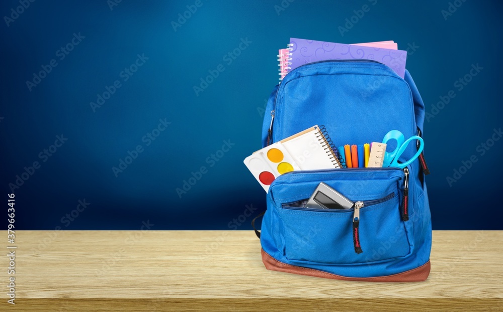 Classic school backpack with colorful school supplies and books on desk.