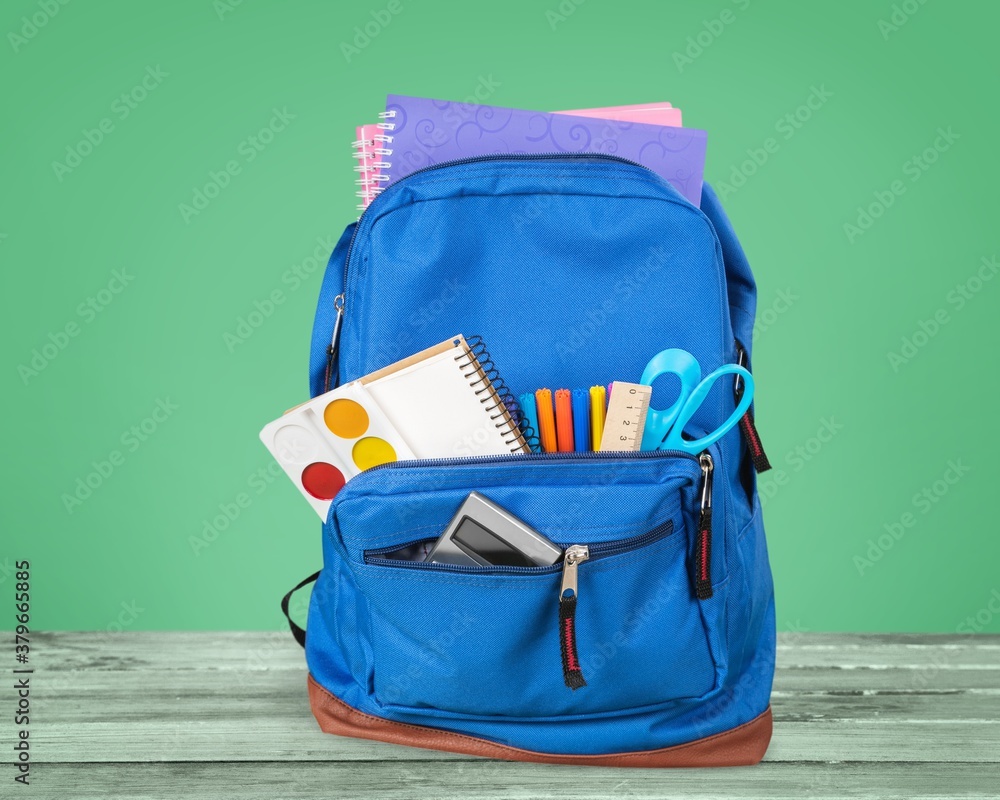 Classic school backpack with colorful school supplies and books on desk.