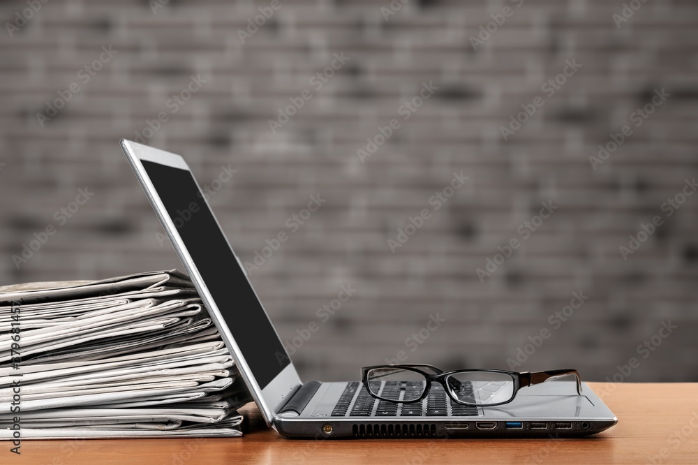 Laptop and newspapers stack on a table with background