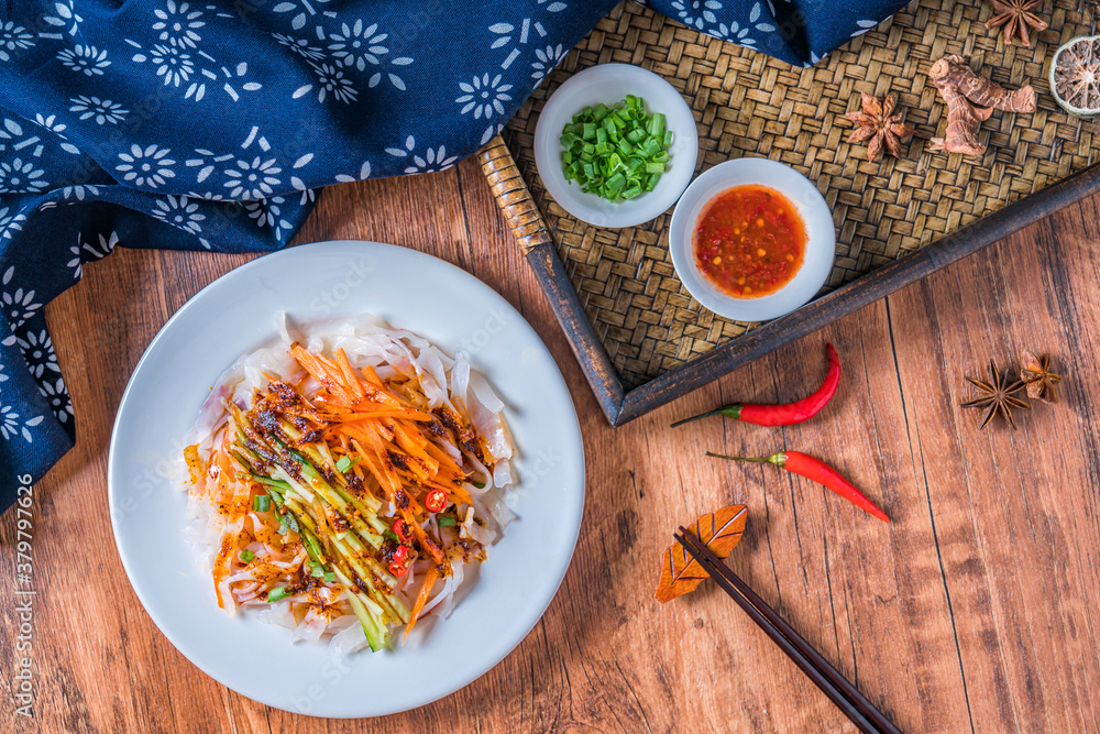 A plate of Shaanxi Qishan spicy cold rice noodles placed on a wooden table