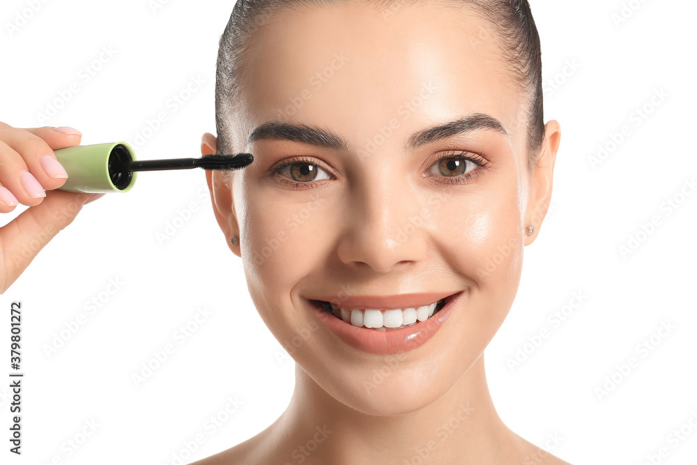 Beautiful young woman applying mascara against white background