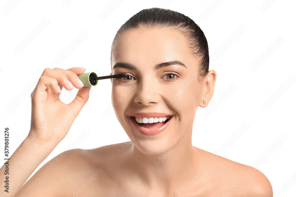 Beautiful young woman applying mascara against white background