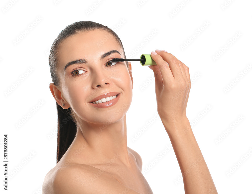 Beautiful young woman applying mascara against white background