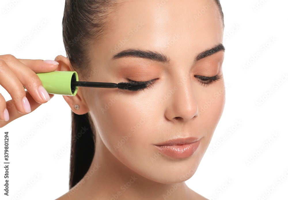 Beautiful young woman applying mascara against white background