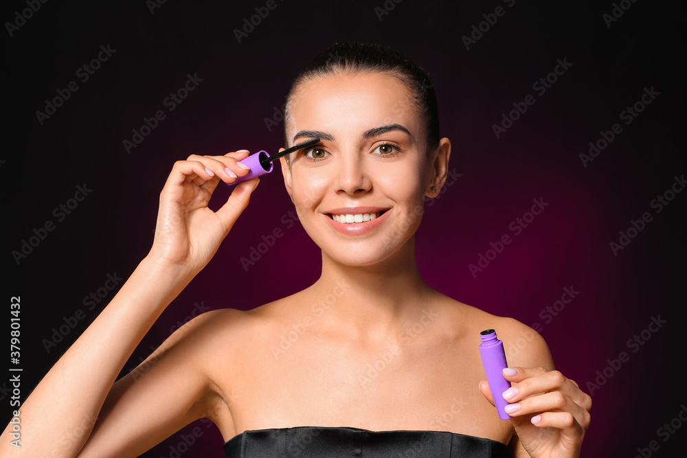 Beautiful young woman with mascara on dark background