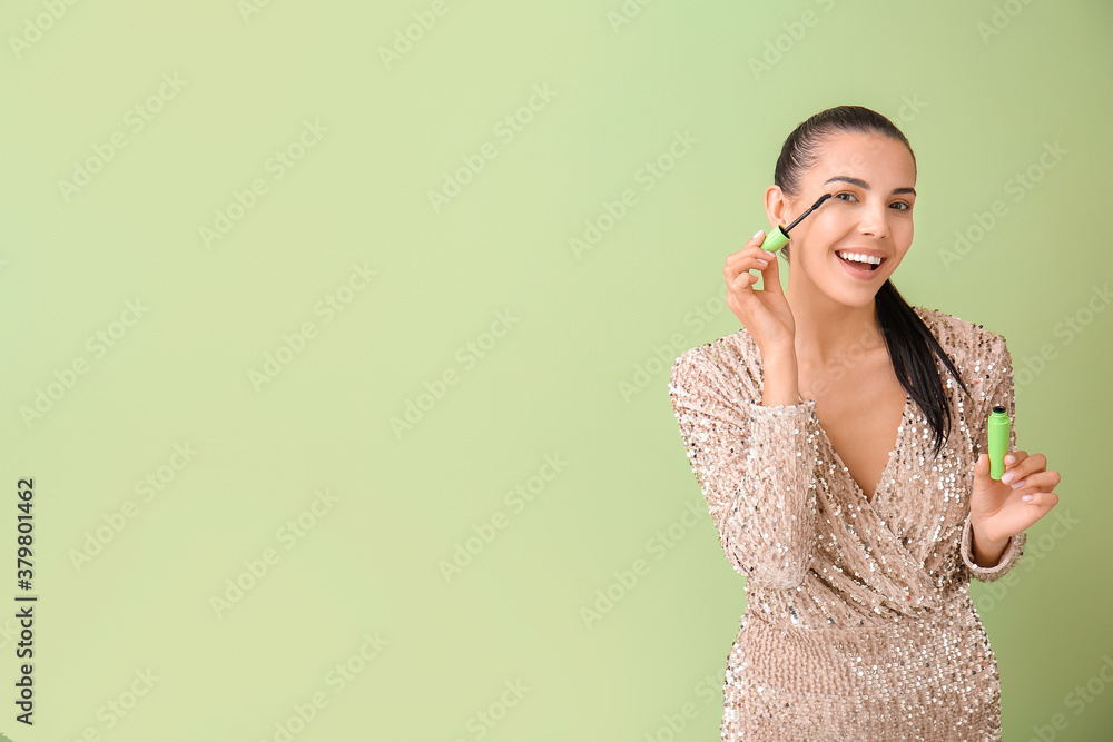 Beautiful young woman applying mascara against color background