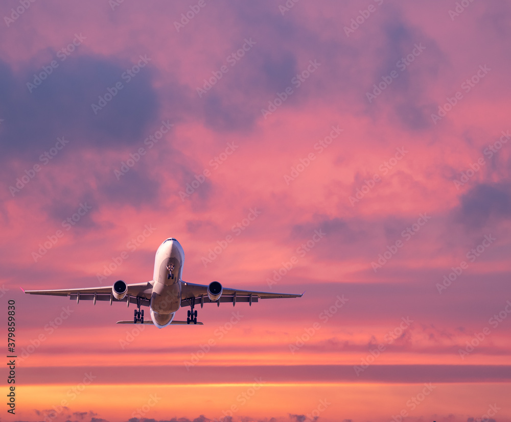 Airplane is flying in colorful sky at sunset. Landscape with white passenger airplane, purple sky wi