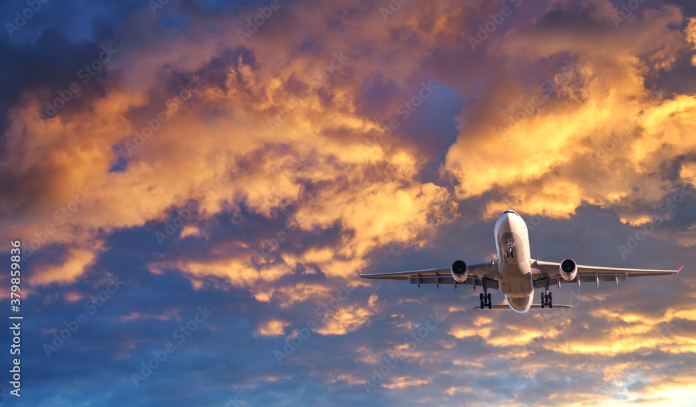 Airplane is flying in colorful sky at sunset. Landscape with white passenger airplane, purple sky wi