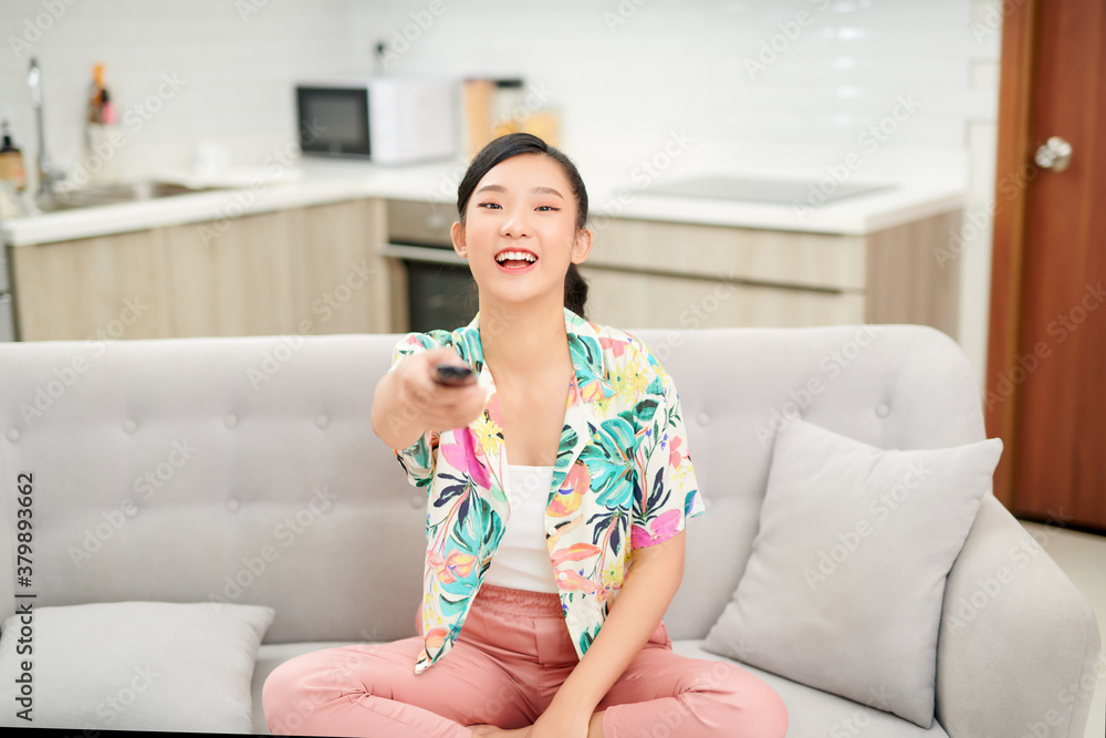 television, relax, home and happiness concept - smiling teenage girl sitting on couch with tv remote