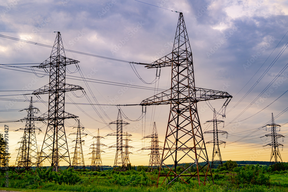 Electricity pylons bearing the power supply across a rural landscape. Orange sunset. Selective focus