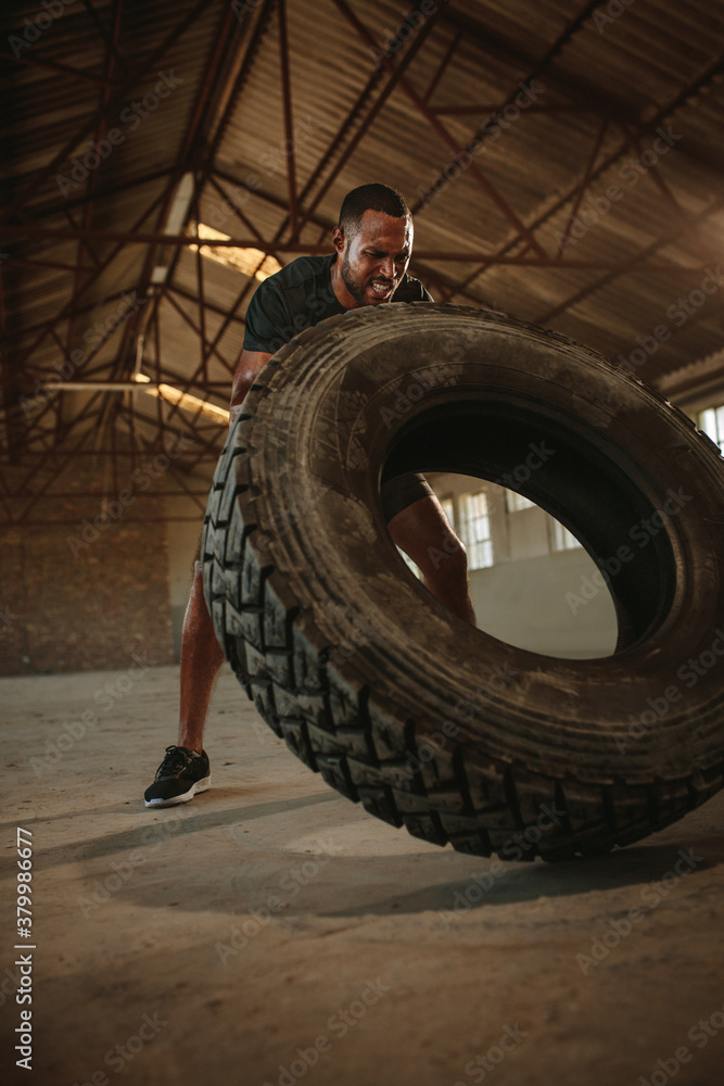 Man doing tire flipping workout at empty warehouse