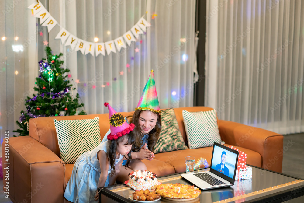 Happy little girl celebrating birthday with her mother at home with father on video call in laptop w