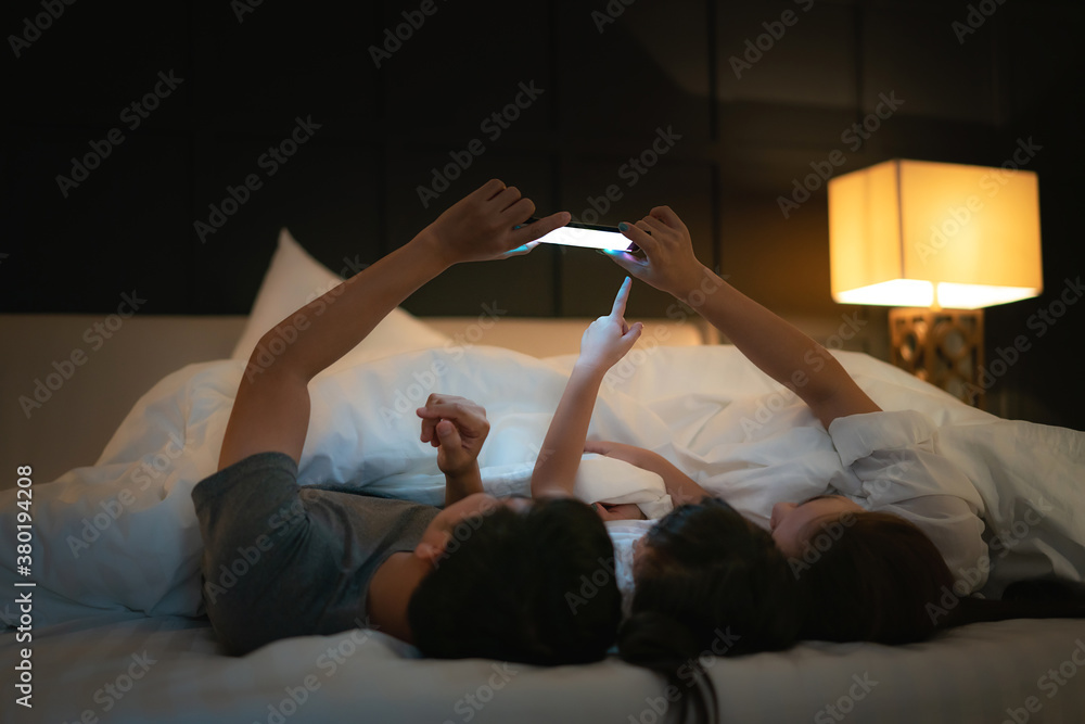 Asian happy family mother, father and little daughter watching movie or cartoon in smartphone togeth