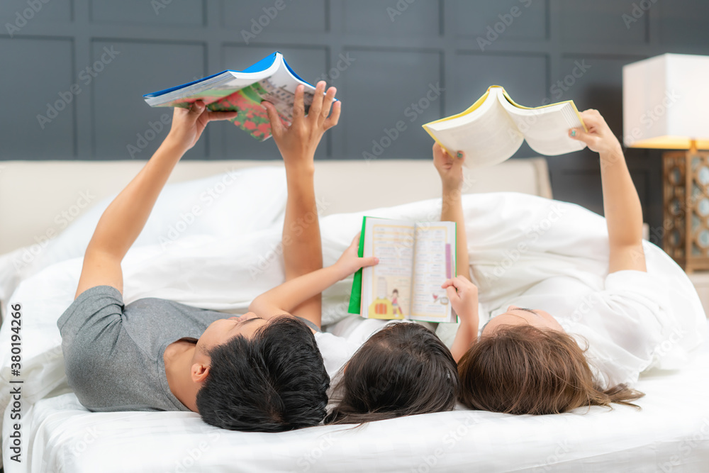 Asian family with father, mother and her daughter reading fairy tail story book on bed at home toget