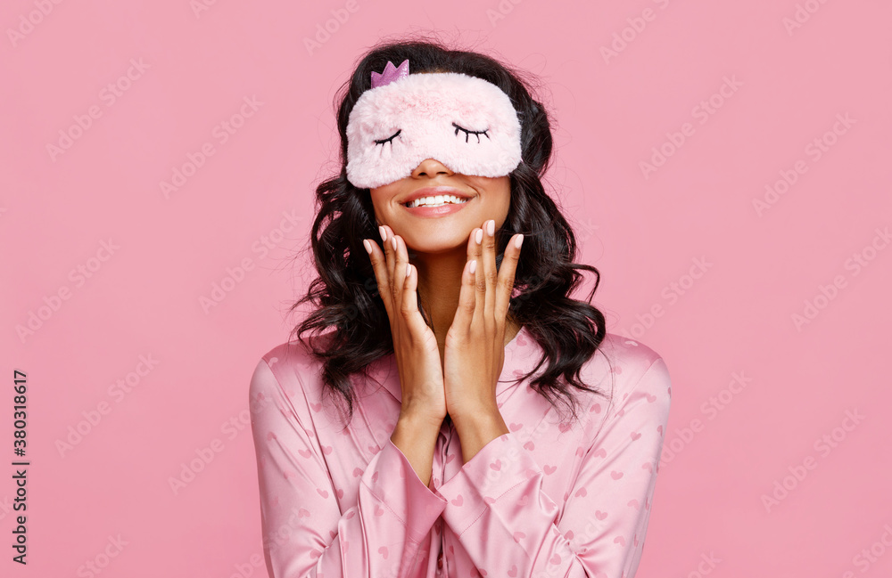 Cheerful ethnic woman applying cream on face before sleep.