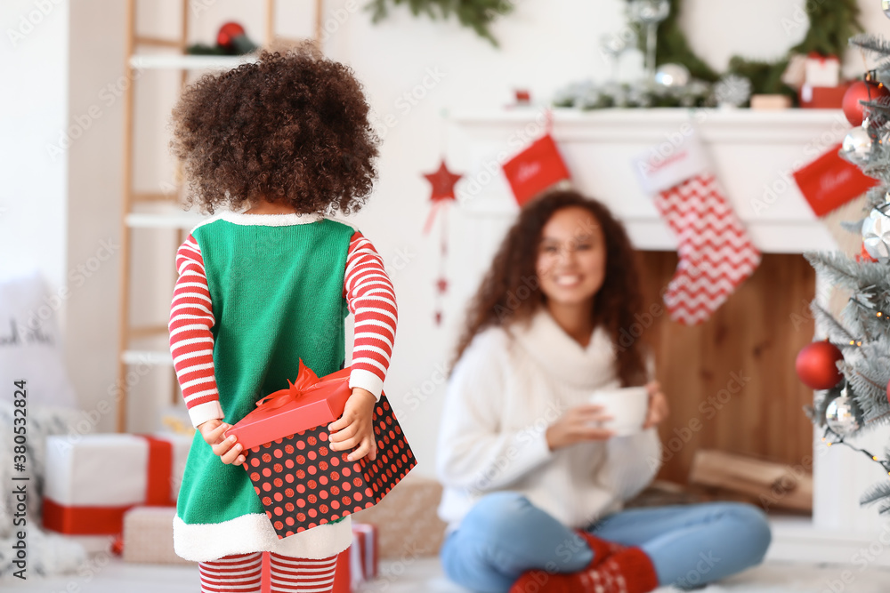 Cute African-American girl hiding gift for her mother on Christmas eve