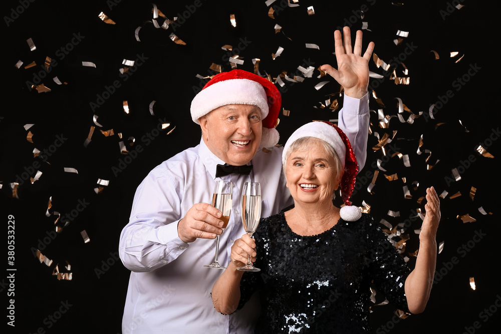 Elderly couple with champagne celebrating Christmas on dark background