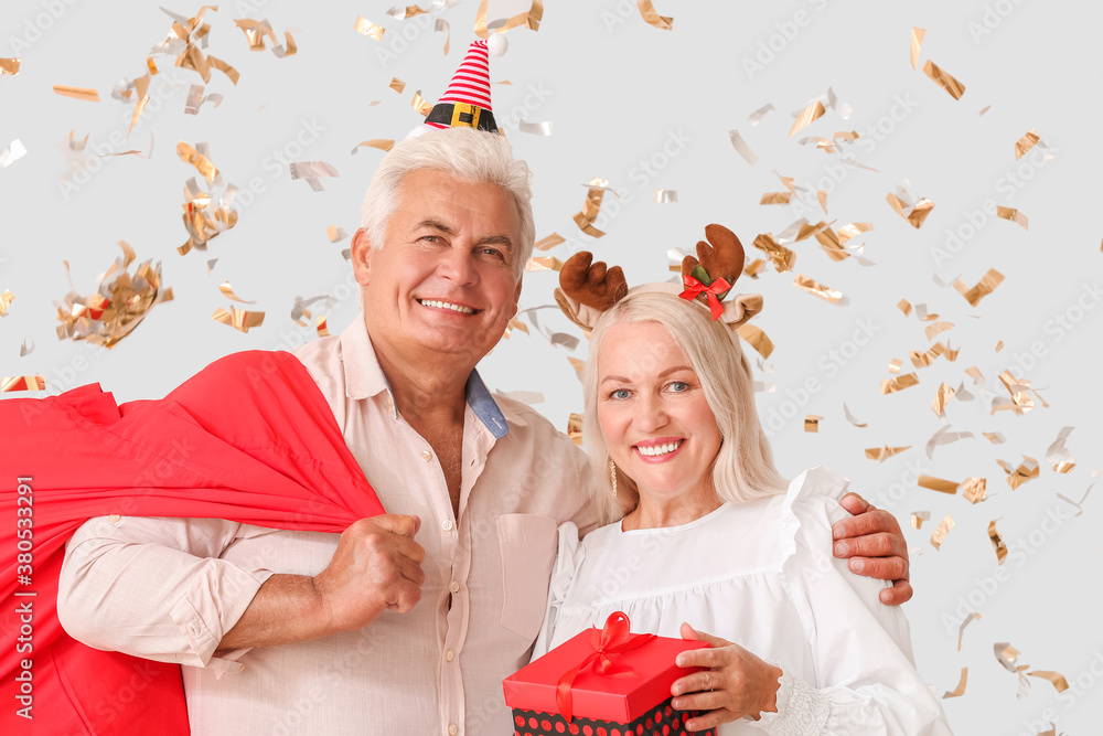 Elderly couple with Christmas gifts on light background