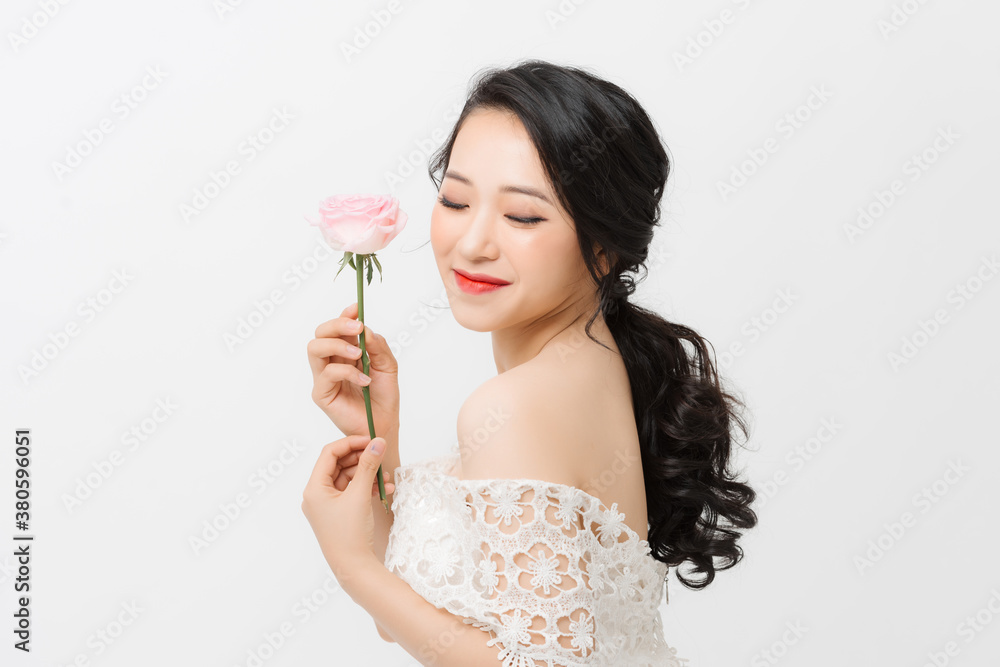 Profile portrait of a beautiful young woman smelling pink rose, isolated on white background.