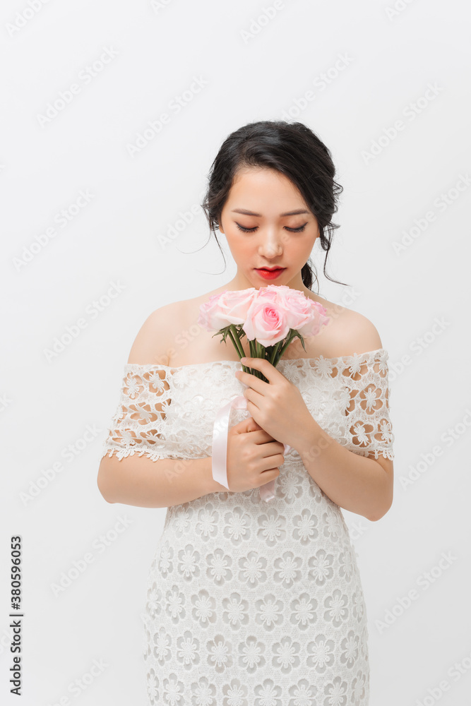 Profile portrait of a beautiful young woman smelling pink rose and looking down, isolated on white b